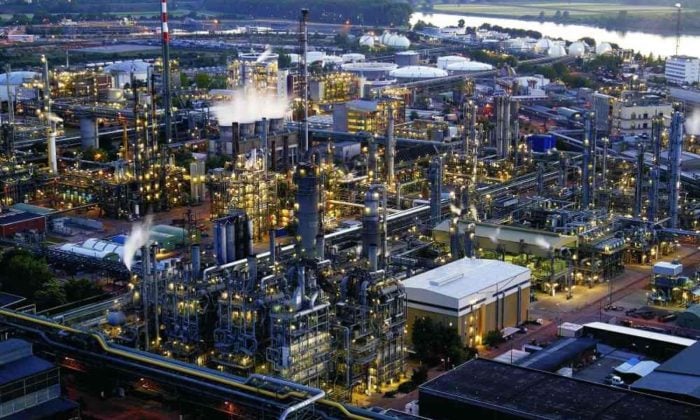 Aerial night view of a chemical processing plant with illuminated distillation towers beside a river