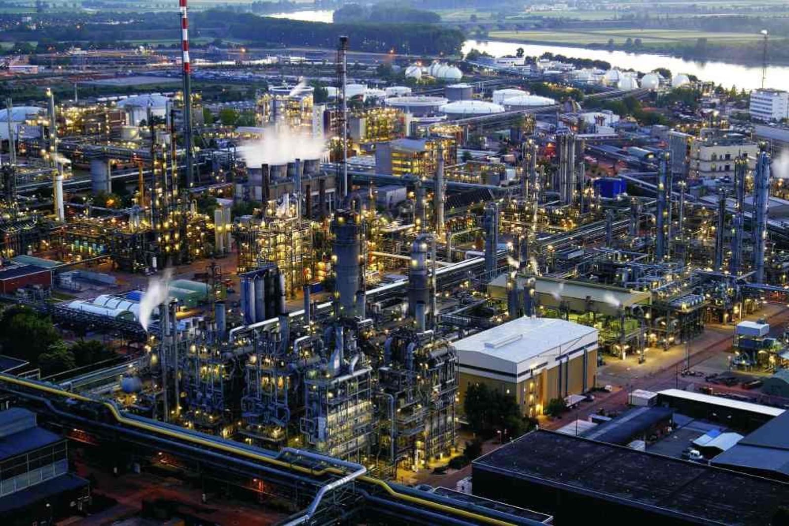 Aerial night view of a chemical processing plant with illuminated distillation towers beside a river